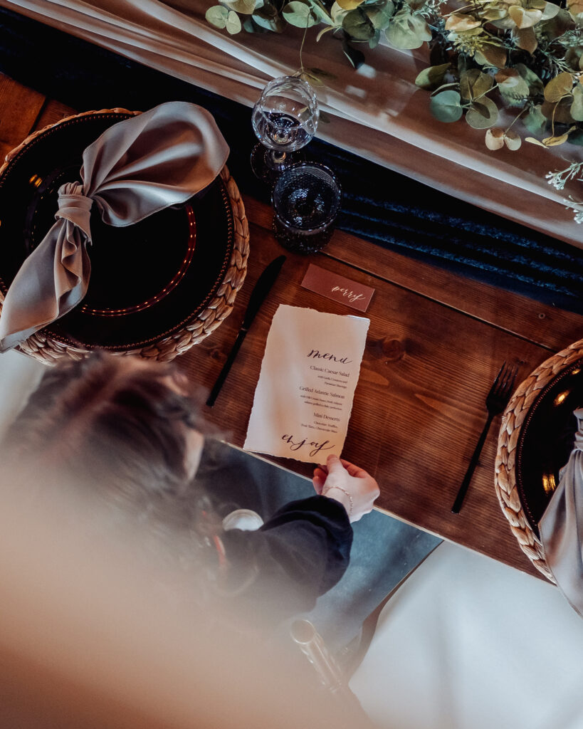 Image showcasing table set with dark elements. Person setting a menu down on the table. 