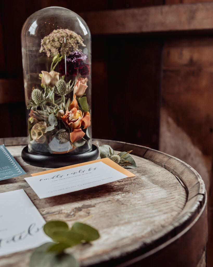 Flower arrangement done in a glass cloche with wedding stationary around it. 