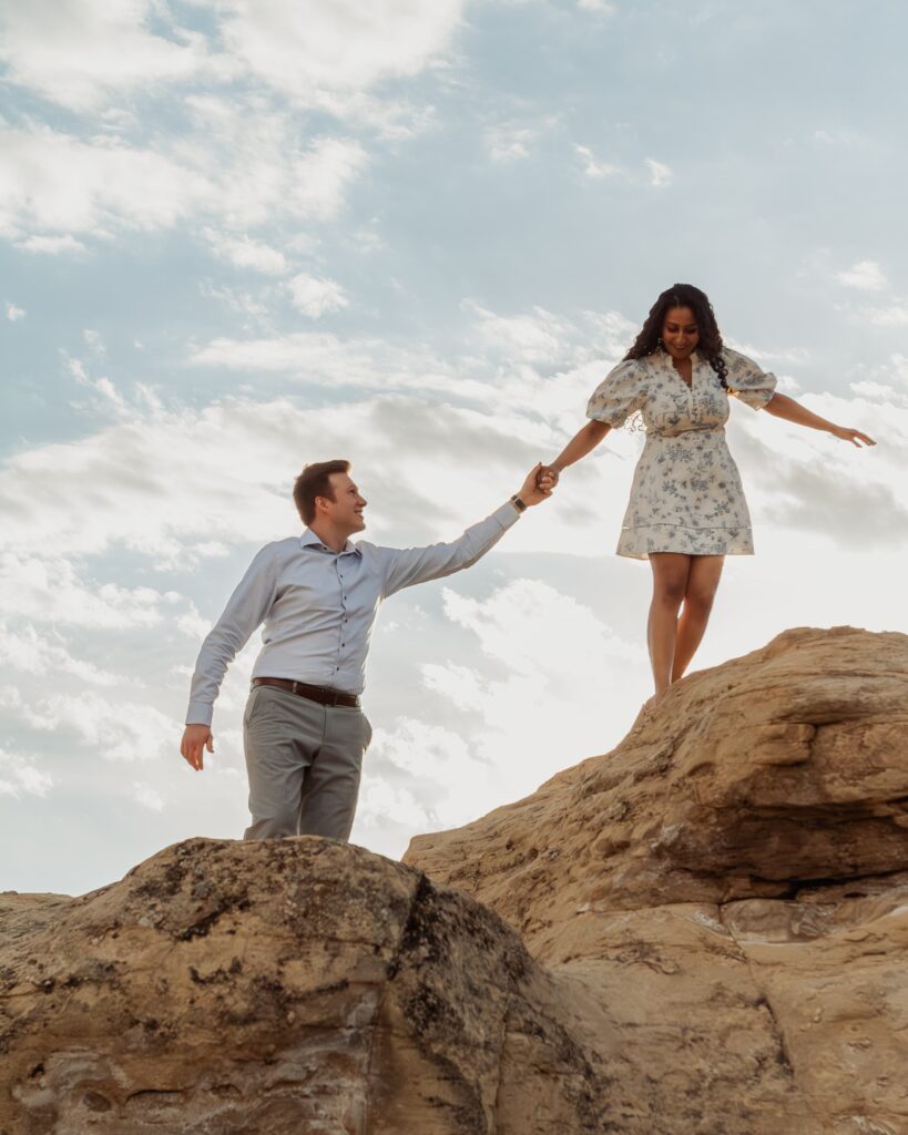 Couple holding hands as he helps her along an edge in Writing-on-Stone Provincial Park.